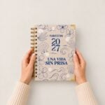 manos sosteniendo agenda de pasta dura Planifesting 2027 beige "Una vida sin prisa" sobre fondo claro