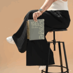 Mujer sentada en banco negro sosteniendo la agenda espiral Planifesting 2026 verde con portada motivadora.