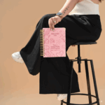 Mujer sosteniendo la Agenda Planifesting 2026 rosa con flores sentada en banco