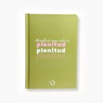 Libreta color verde con la frase "Manifiesto una vida en plenitud" en tipografía rosa y blanca.
