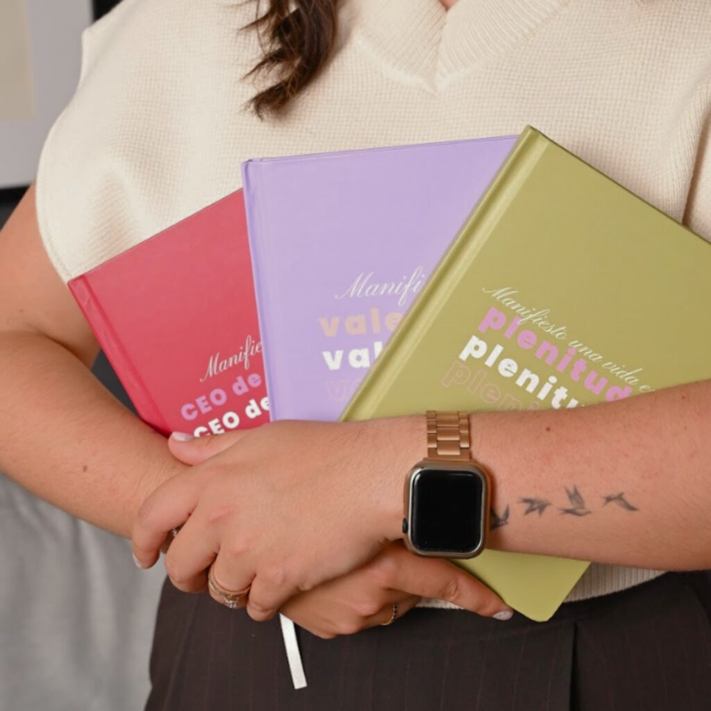 Persona sosteniendo tres libretas para notas de pasta dura en colores rojo, morado y verde, diseño premium