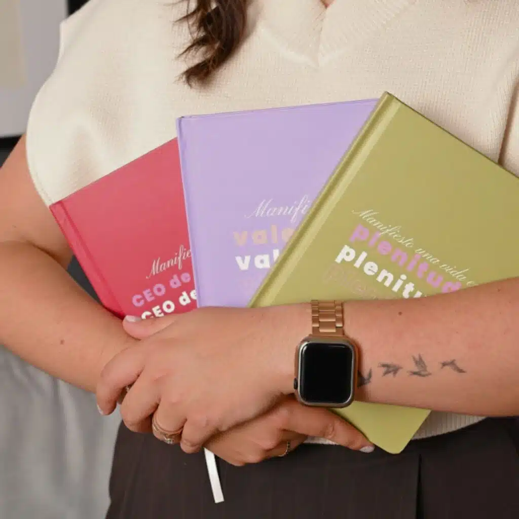 Persona sosteniendo tres libretas para notas de pasta dura en colores rojo, morado y verde, diseño premium