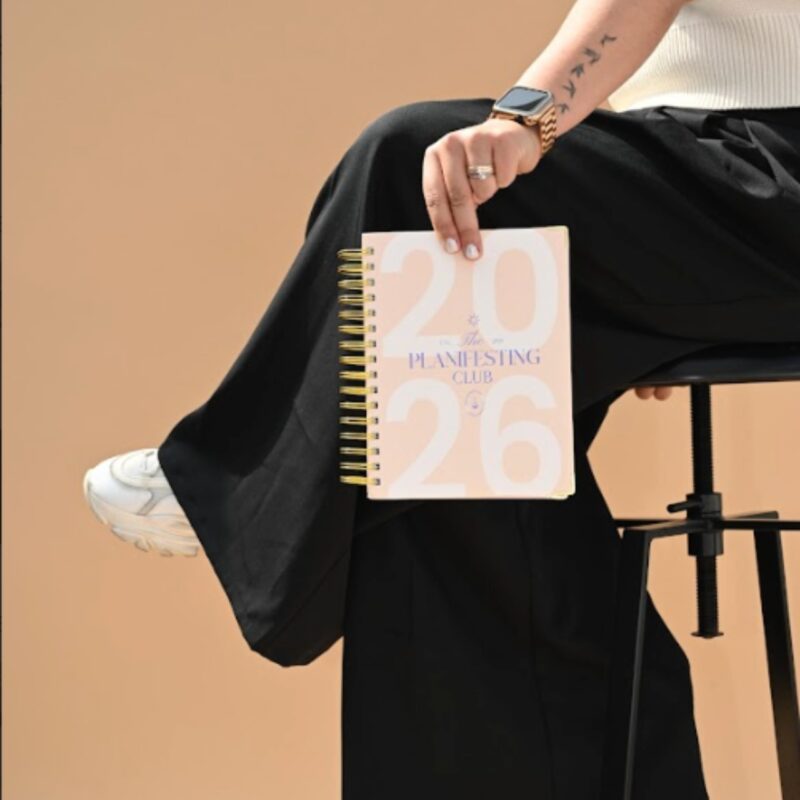Agenda espiral Planifesting 2026 rosa con morado en mano de chica sentada en un banco, foto lifestyle.