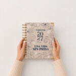 Manos sosteniendo la agenda de pasta dura Planifesting 2027 beige "Una vida sin prisa"