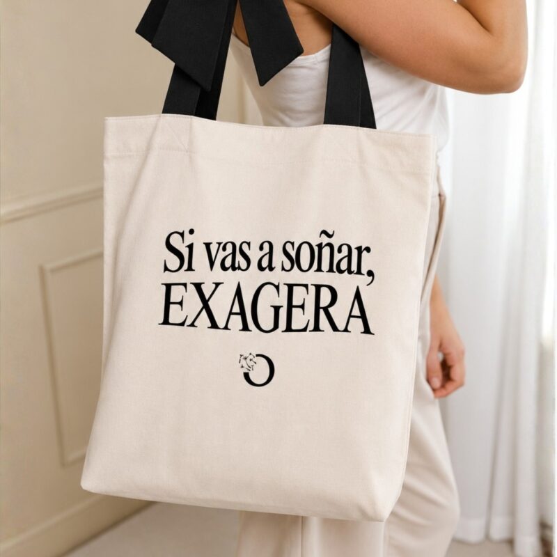 Mujer cargando el tote bag de tela cruda "Si vas a soñar, exagera" con asa de moño negro